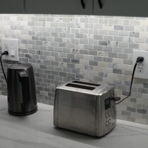 Kitchen countertop with a marble backsplash featuring two modern electrical outlets, one powering a toaster and another a kettle.