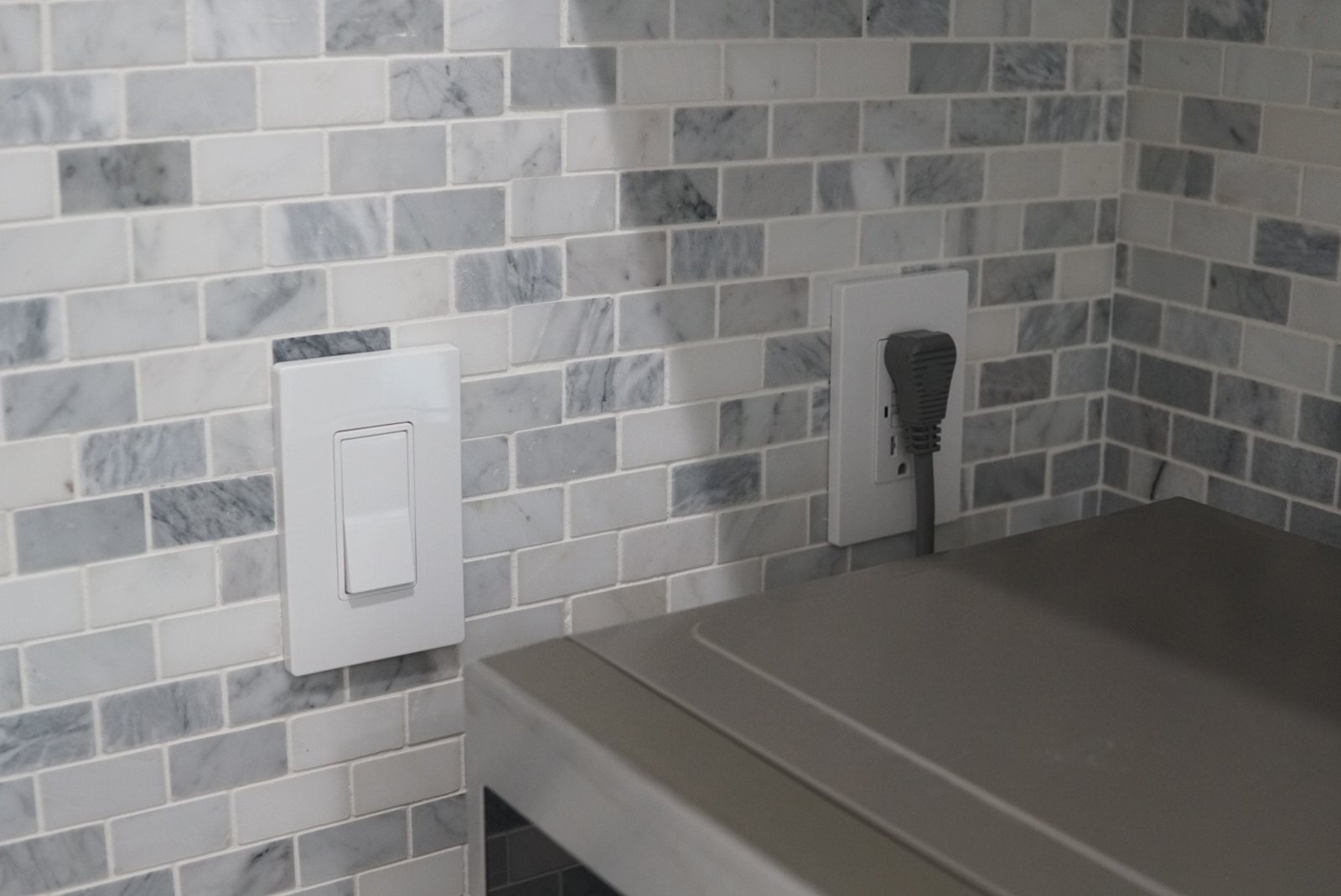 Modern electrical outlet and light switch installed on a marble backsplash in a stylish kitchen setting.