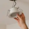 Hand removing recessed ceiling light fixture during electrical uninstallation.